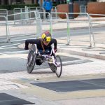 A dedicated athlete competes in a marathon using a racing wheelchair on city streets.