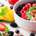 A vibrant bowl filled with fresh berries, mango, almonds, and herbs, perfect for a healthy snack or breakfast.