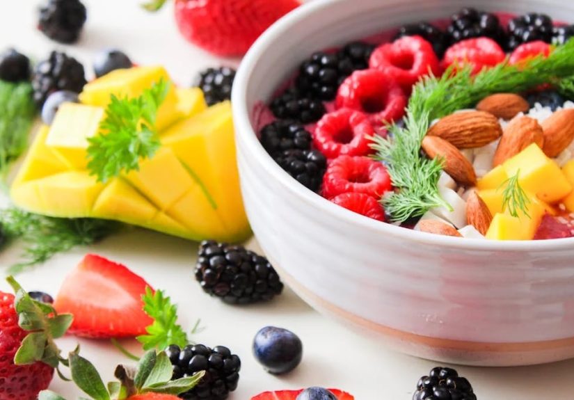 A vibrant bowl filled with fresh berries, mango, almonds, and herbs, perfect for a healthy snack or breakfast.