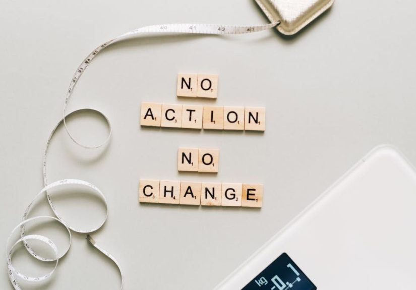 Motivational concept with scrabble tiles spelling no action no change alongside a measuring tape and scale.